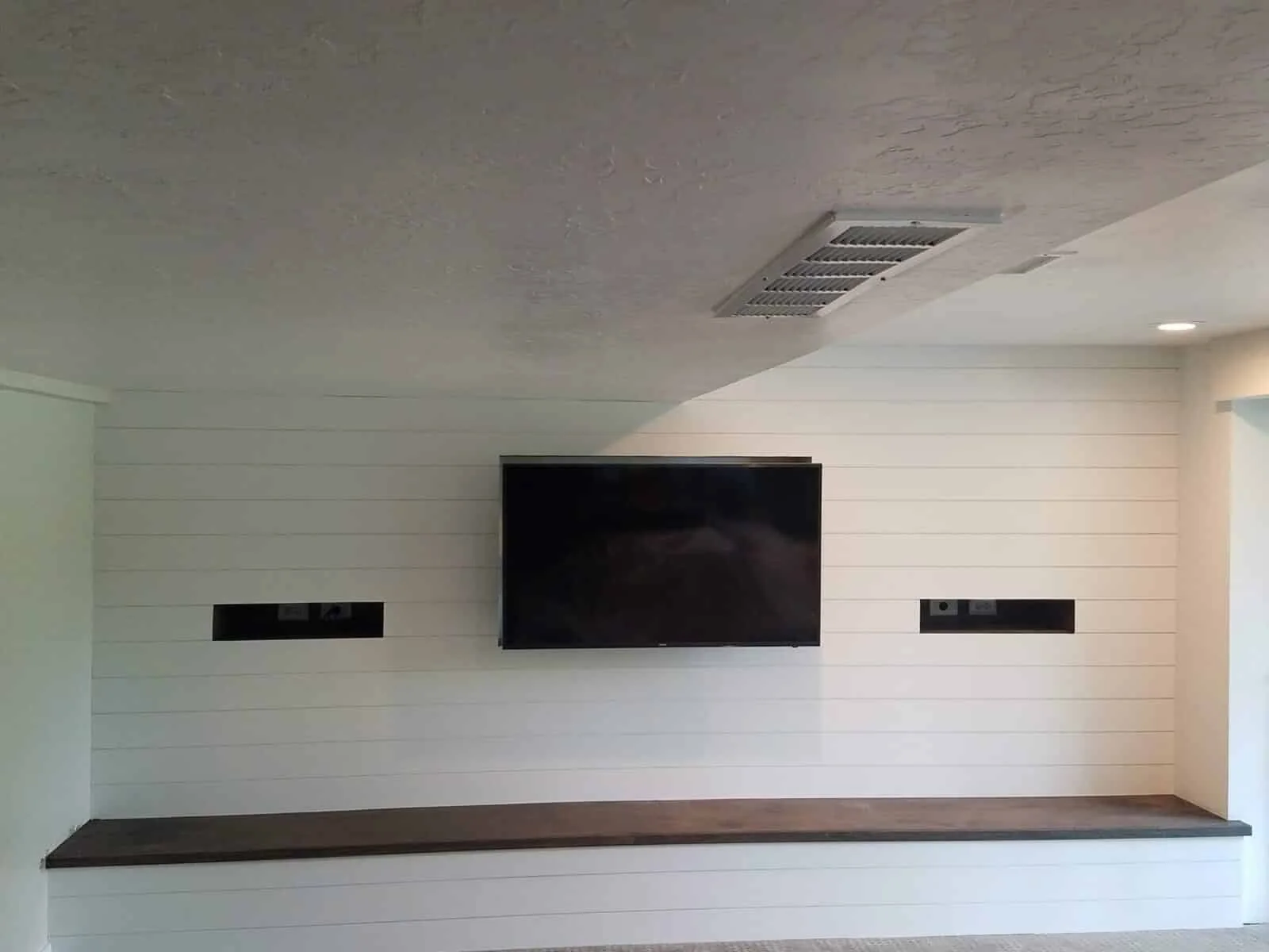 TV, speakers, and floating shelf aligned on a paneled feature wall